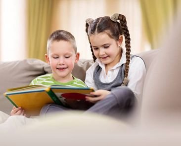 Smiling siblings sitting at home and reading a book together.